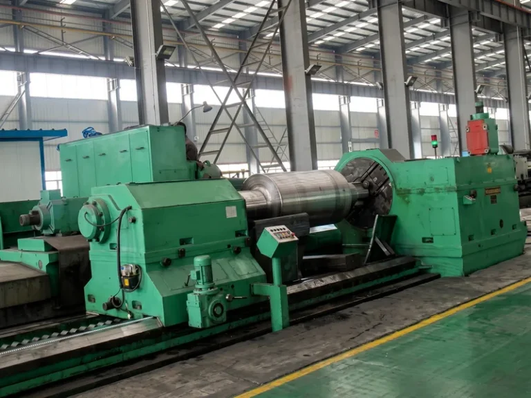 A massive Duron heavy-duty CNC roll grinder performing precision grinding on a large steel mill roll, with coolant mist, showcasing our state-of-the-art precision engineering capabilities in our manufacturing workshop.