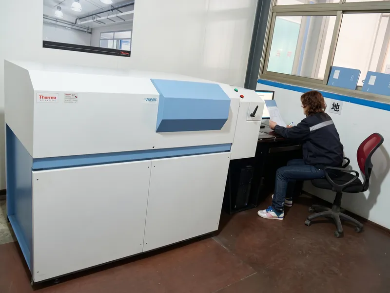 Technician operating a Thermo Scientific optical emission spectrometer (OES) for exact chemical analysis of mill roll steel heats.